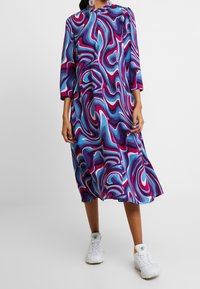 Kolorowa sukienka z długim rękawem o wirującym wzorze w odcieniach fioletu, niebieskiego i różowego. Wykonana z tkaniny o gładkiej strukturze; o długości do kolan.