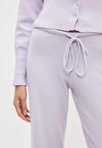 Ανοιχτό μωβ παντελόνι με κορδόνι στη μέση, κατασκευασμένο από μαλακό υλικό. Διακρίνονται επίσης ριμπ μανσέτες και ένα ταιριαστό ριμπ τοπ.