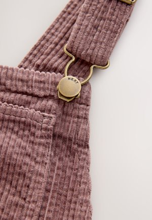 Salopette con bretelle in velluto a coste color rosa polveroso, con costine verticali, fermaglio in ottone con incisione "NEXT" e dettaglio tasca frontale.