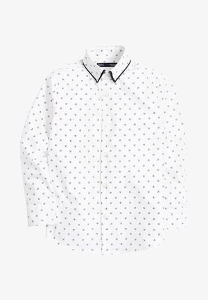 Chemise blanche à boutons avec petits motifs croix noirs, col bordé de noir, manches longues et fermeture boutonnée devant.
