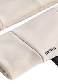 Beżowy materiałowy pokrowiec na laptopa o gładkiej fakturze, z widocznym przeszyciem i logo „OYSHO” w czerni po boku.