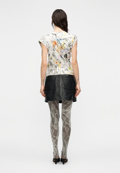 Γραφικό βαμβακερό T-shirt με κοντά μανίκια καπέλου· φορεμένο πάνω από μαύρη δερμάτινη μίνι φούστα. Πόδια με καλσόν σε γκρι φιδίσιο σχέδιο και μαύρες γόβες.