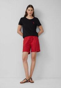 Zwarte katoen t-shirt met ronde hals en rode hartborduursel, gecombineerd met rode shorts met elastische tailleband en omgeslagen mouwen.
