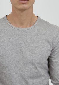 Grå langermet skjorte laget av myk stoff, med rund hals og enkelt design med synlige sømdetaljer.