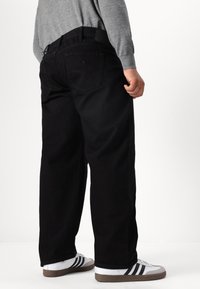 Jeans negre, cu croi lejer, dintr-o țesătură netedă de denim, cu bucle pentru curea și două buzunare în spate, asortați cu teniși albi cu dungi negre.