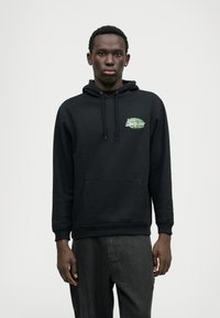 Hanorac negru cu buzunar frontal tip kangaroo, glugă cu �șnur și accente grafice verzi pe piept. Țesătura pare moale, cu o croială clasică.