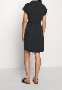 Abito in cotone nero con maniche corte, vita stretta e silhouette dritta. Presenta un colletto e una consistenza leggera.