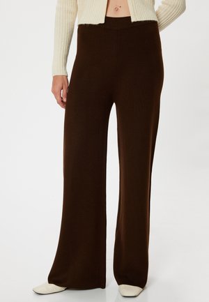 Bruine, wijde broek van een textuurstof met een hoge taille. Gepaarde met lichte schoenen en een ribbeltrui in crème.