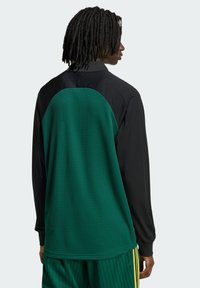Majica s dugim rukavima s crnim prednjim dijelom i teksturiranim zelenim stražnjim dijelom. Dizajn uključuje zaobljeni, kontrastni kroj na ramenima.