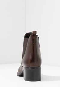 Stivale alla caviglia in pelle marrone con pannelli elastici laterali, punta tondeggiante e un modestissimo tacco nero. Texture liscia e design minimalista.