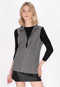 Gilet in pile grigio con colletto alto e zip frontale completa, indossato su una maglietta nera a maniche lunghe, caratterizzato da un design semplice e una texture morbida.