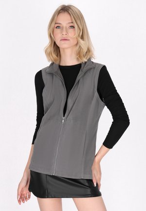 Vest din fleece gri, cu guler înalt și fermoar pe toată partea din față, purtat peste un top negru cu mâneci lungi, având un design simplu și o textură moale.