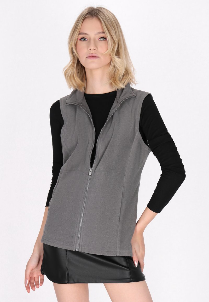 Gilet in pile grigio con colletto alto e zip frontale completa, indossato su una maglietta nera a maniche lunghe, caratterizzato da un design semplice e una texture morbida.