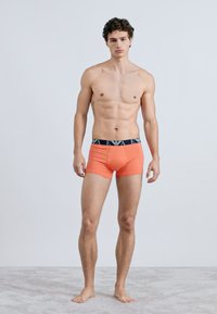Boxers laranja com cós azul-marinho com marca subtil, feitos de tecido macio e elástico para conforto e ajuste.