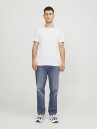 Hvid bomulds t-shirt med rund hals, parret med blå denimjeans. Modellen har grå og sorte træningssko på. Enkel, afslappet design.