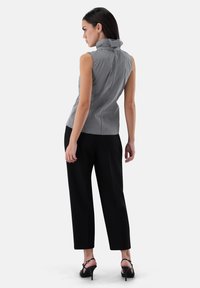 Sleeveless checkered top with high collar, fitted design, and back button closure. Worn with black pants and strappy high heels.