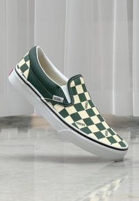 Grüne und cremefarbene Karomuster Slip-On Vans Sneaker mit weißer Sohle und Branding-Akzenten. Glatter Textil-Obermaterial, schlankes Design.