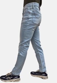 Jeans di denim azzurro chiaro con una vestibilità slim, cinque tasche e dettagli di cucitura evidenti. Indossati con sneakers sportive bianche e nere.