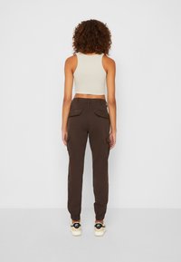 Bruine cargobroek met elastische boorden en zijzakken, gecombineerd met een lichtgekleurde cropped tanktop. De textuur lijkt glad en aansluitend.