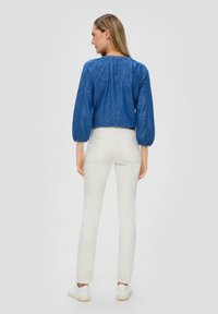 Niebieski krótki top z denimu z bufkami, zestawiony z dopasowanymi białymi spodniami. Model nosi białe sneakersy. Prosty, czysty design.