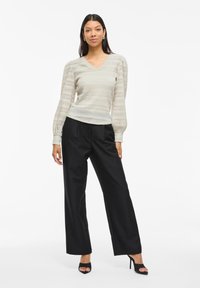 Light gray textured knit sweater with puffed sleeves paired with high-waisted black wide-leg trousers and black heeled sandals.