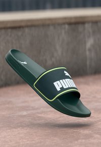 Sandale verte en plastique avec une sangle texturée, arborant un logo "PUMA" blanc et des accents jaunes. Semelle lisse conçue pour le confort.