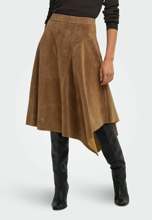 Femme portant une jupe asymétrique en daim marron avec un pull côtelé noir et des bottes en cuir noires montant jusqu'aux genoux.