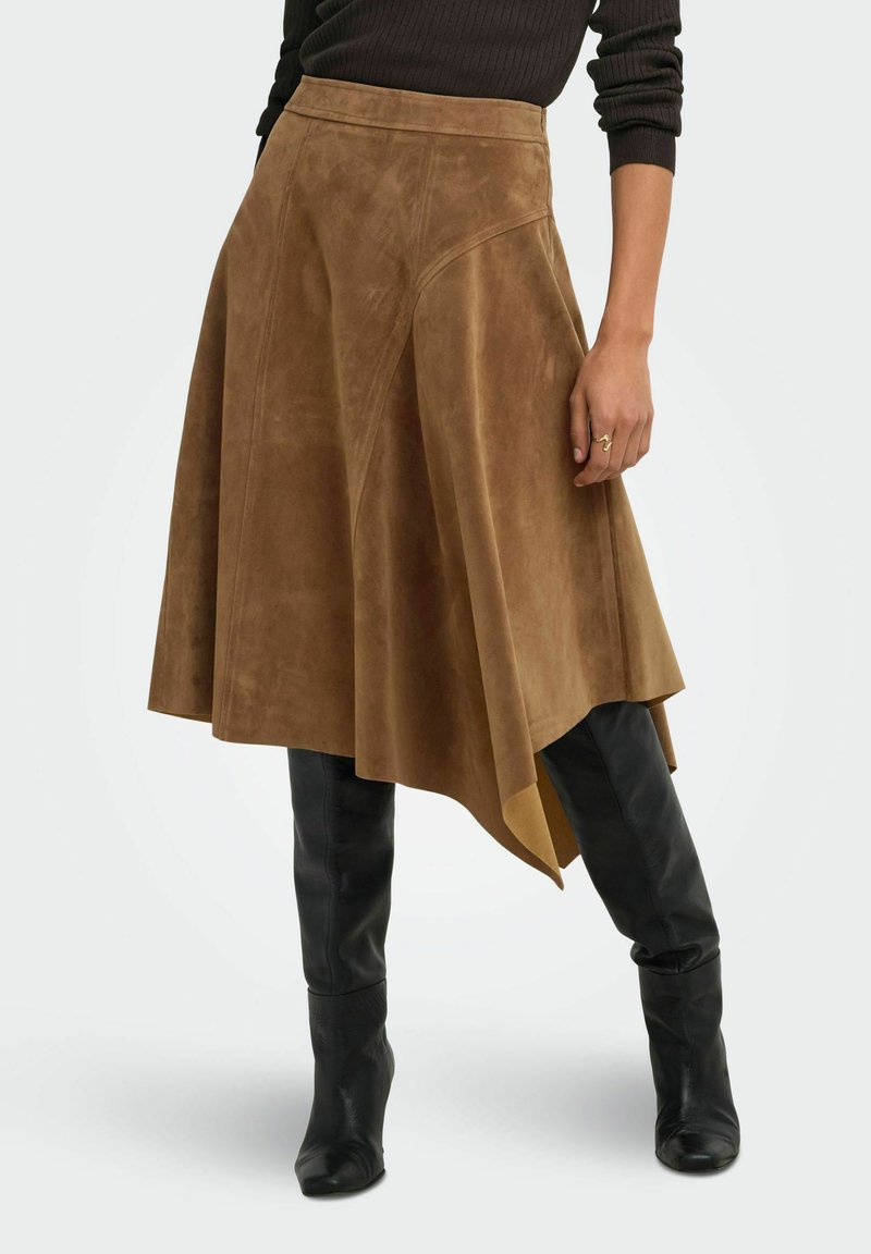 Femme portant une jupe asymétrique en daim marron avec un pull côtelé noir et des bottes en cuir noires montant jusqu'aux genoux.