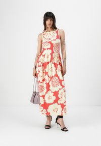 Maxi dress with red and yellow floral pattern, sleeveless design, flared skirt, cotton-like texture, paired with black heels and a gray bag.
