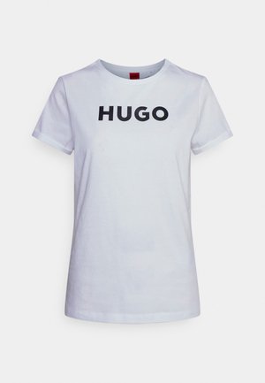 Biały T-shirt z krótkim rękawem i okrągłym dekoltem z czarnym tekstem "HUGO" zapisanym wielkimi literami, wyśrodkowanym na przodzie.