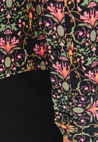 Kwiatowa koszula z guzikami na czarnym tle, z różowymi i zielonymi wzorami botanicznymi, teksturowana tkanina i czarne guziki.