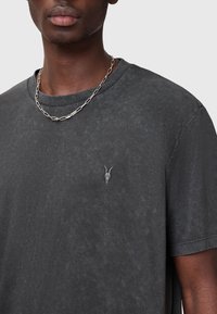 Mörkgrå kortärmad T-shirt med en subtil skallelogotyp på bröstet, tillverkad av ett texturerat tyg med en avslappnad passform. Silverkedja ingår.