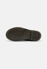 Pohja tummanruskeasta saappaasta ylös päin, jossa näkyy tekstuuri ja kuviointi sekä neliömäinen brändäysohjaus keskellä.