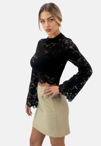 Sort blonde langærmet top med bølgede kanter, parret med en beige tætsiddende miniskørt med en frontknapdetalje.