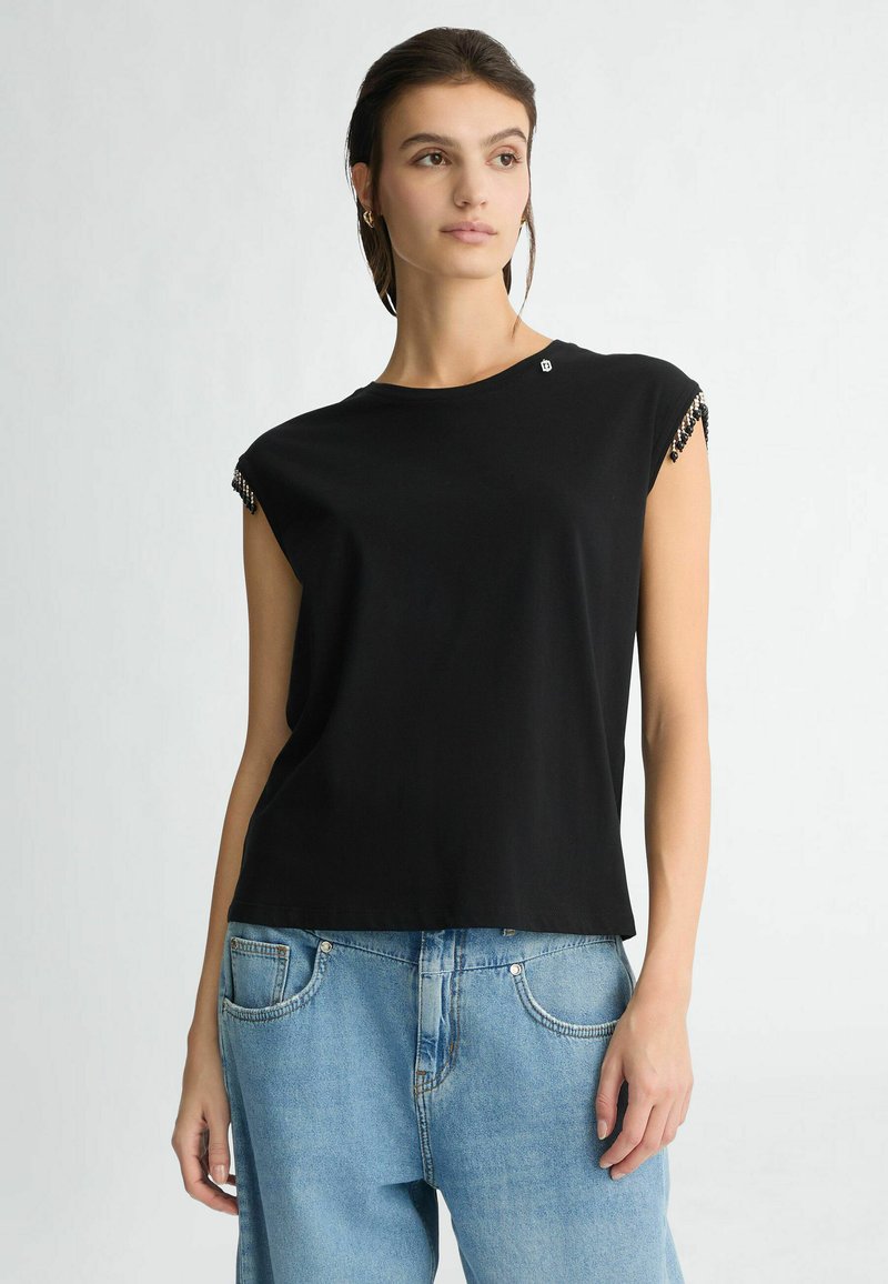 T-shirt in cotone nero con maniche a cappuccio, caratterizzato da dettagli di perline sulle spalle. Abbinato a jeans in denim blu chiaro.