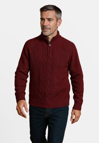Bordeaux gebreide trui met een kwart rits, voorzien van een gewatteerd kabelpatroon en geribde manchetten en zoom. Combineert goed met donkerblauwe spijkerbroek.