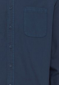 Marineblå skjorte med knapper, med brystlomme og synlige sømmer på lommen og knappestolpen.