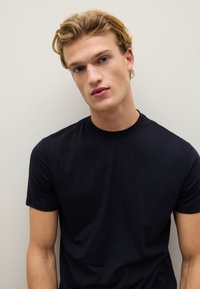 Camiseta negra de manga corta hecha de tela suave. Escote redondo y diseño ajustado, exhibida sobre un fondo claro liso.