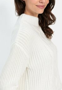 Weißer gestrickter Pullover mit hochgeschlossenem Kragen, der vertikale Rippstrickmuster und dezente Zopfdetails aufweist, mit lockerer Passform und strukturiertem Finish.