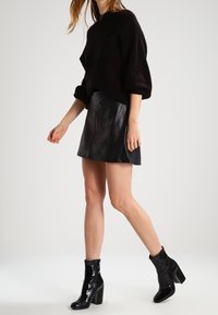 Pullover oversize nero con texture abbinato a una mini gonna in pelle nera elegante. Stivaletti neri lucidi completano l'outfit.