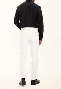 Schwarzes Langarmhemd mit entspannter Passform, kombiniert mit weißen maßgeschneiderten Hosen und schwarzen eleganten Schuhen, die ein glattes Finish und Manschetten aufweisen.