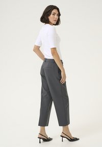 Sive prilagođene hlače visokog struka s suženim nogavicama, uparene s uskim bijelim topom. Crne slingback štikle upotpunjuju outfit.