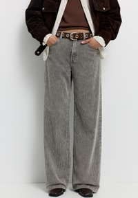 Grijze losse corduroy broek met verticale strepen en een hoge taille. Gecombineerd met een bruine riem en donkere schoenen.