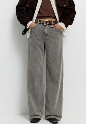 Grijze losse corduroy broek met verticale strepen en een hoge taille. Gecombineerd met een bruine riem en donkere schoenen.