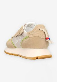 Tan suède sneaker met groene stikselaccenten, een geribbelde rubberen zool en een uniek vetersysteem met kleurrijke kraaldetails.