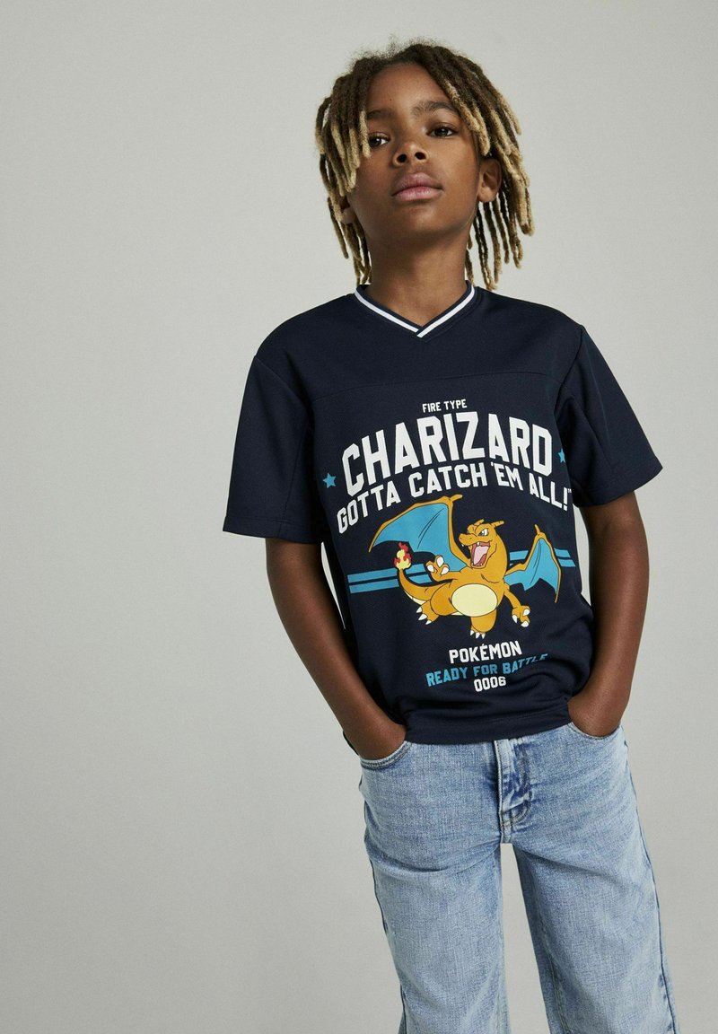 Camiseta gráfica azul marino con Charizard, texto "Tipo Fuego" y "¡Consíguelos Todos!", con mangas cortas y un escote de color contrastante.