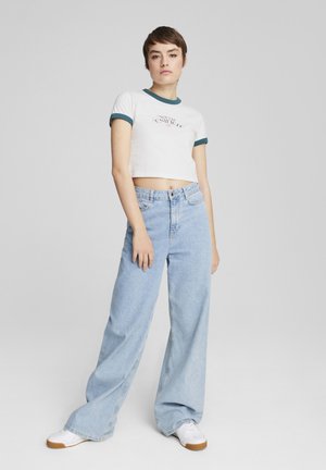 T-shirt blanc court avec des finitions turquoise et un graphique "United", associé à un jean large bleu clair et des baskets blanches avec une semelle en gomme.