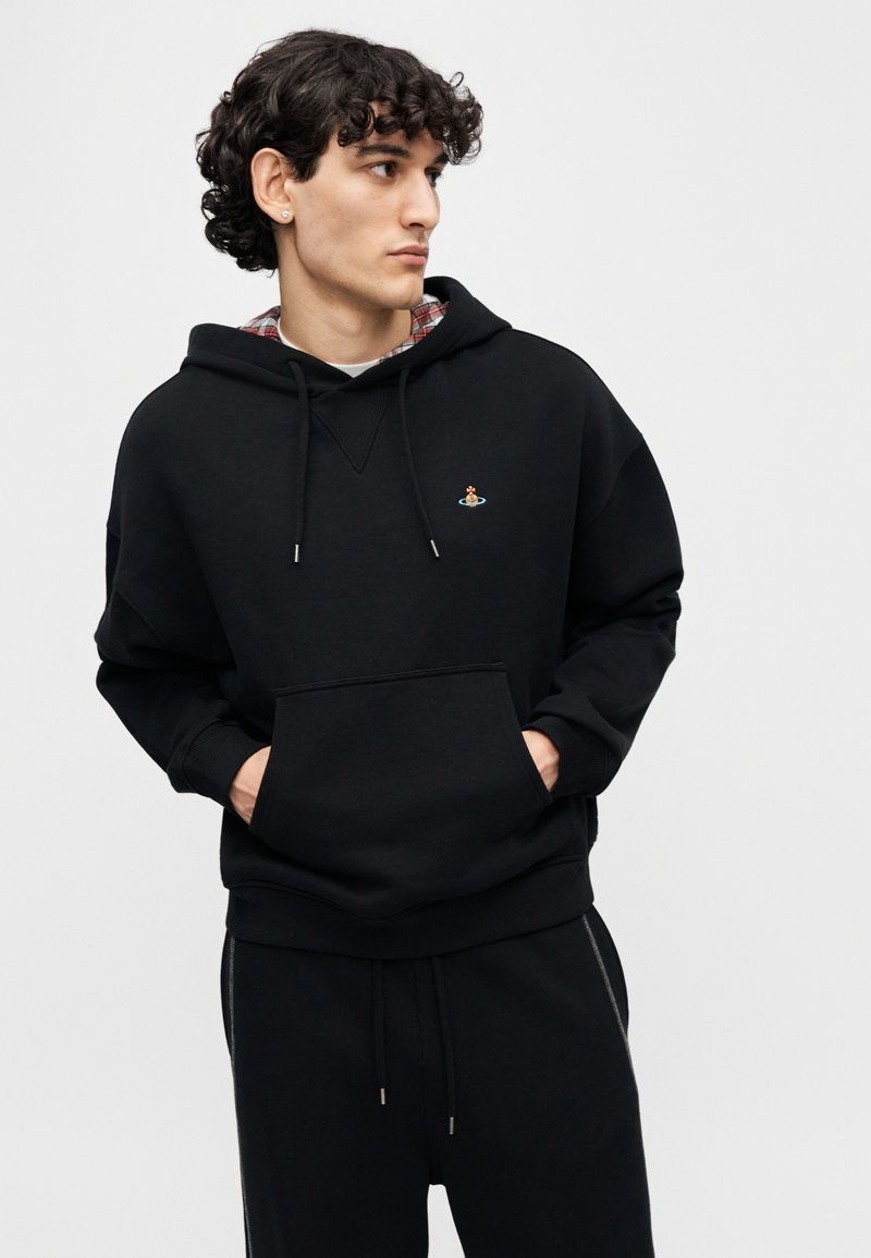 Sweat à capuche noir avec une poche avant, un col en V et un petit logo brodé. Texture douce, porté avec un pantalon de jogging noir assorti.
