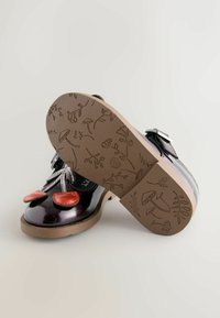 Schwarze und burgunderfarbene Lacklederschuhe mit roten Akzenten, silbernen Schnürsenkeln und einer braunen strukturierten Sohle mit floralen Gravuren.