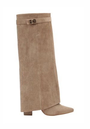 Botte beige en daim montant jusqu’au genou, avec un talon bloc, un bout pointu et une bride décorative avec une boucle dorée près du haut.